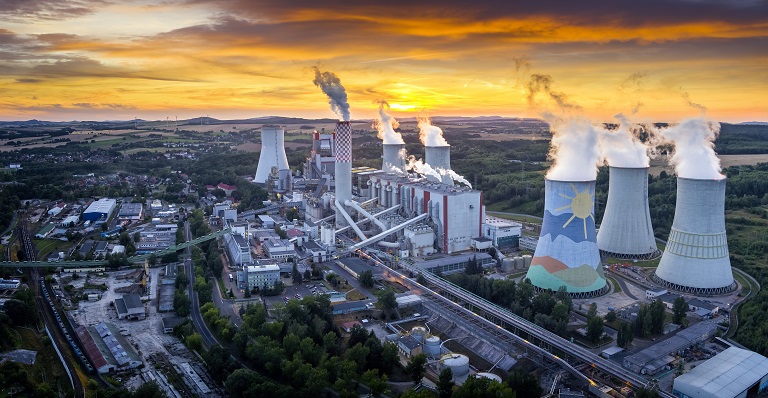 Industrial factory emits smoke with dramatic sunset in background.