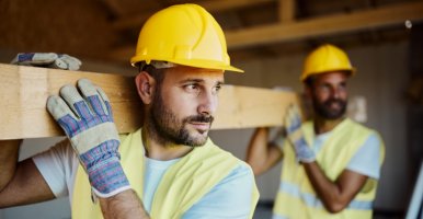 Construction workers carry wooden beam on site.