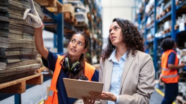 Warehouse worker pointing at rack with a businesswoman holding a clipboard.