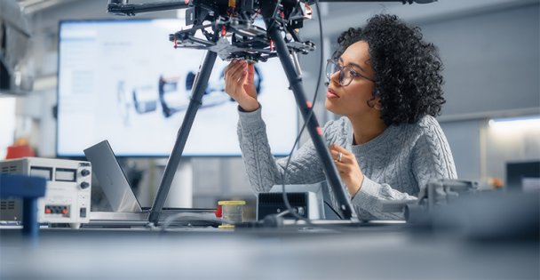A black woman in tech is inspecting the bottom of a robotic innovation