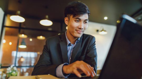 A businessman sitting at a desk scrolling on his laptop.