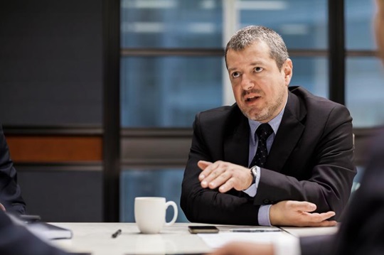 A man sits at a boardroom table, explaining his ideas.