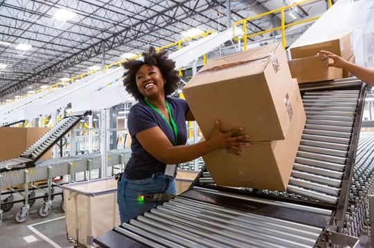 In a warehouse, a joyful woman places boxes on a conveyer.