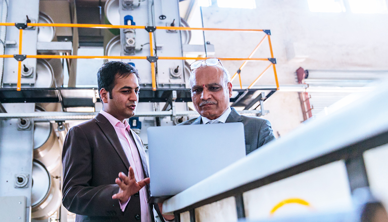 Senior businessman with his factory manager reviewing progress report on a laptop