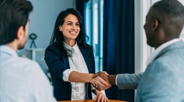 Une femme d’affaires et un homme d’affaires se serrent la main dans un bureau et un autre homme d’affaires se tient à proximité, observant l’interaction.