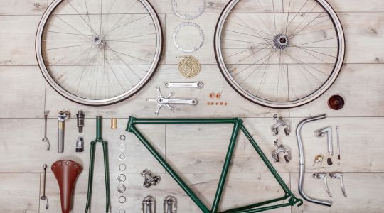 A bicycle frame and components laid out on wooden floorboards.