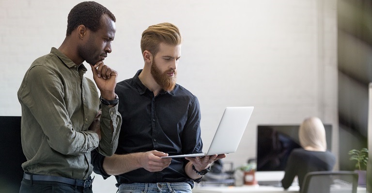 Two worried businessmen look at laptop while standing in an office