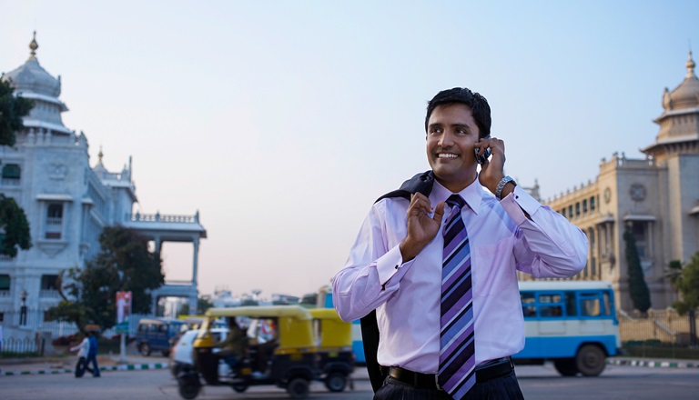 Happy India businessman uses cellphone while walking in busy street