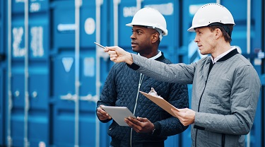 Two men in hard hats stand in front of blue shipping containers
