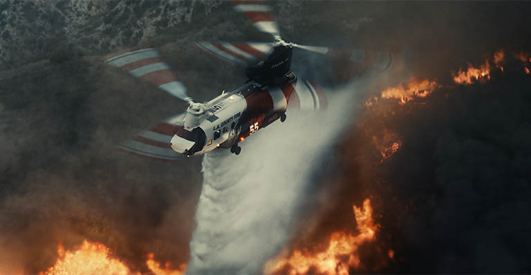 A Coulson Aviation aircraft flying over a raging forest fire below