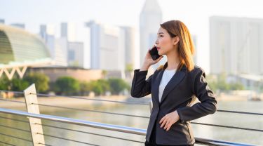 Singaporean businesswoman talks on cellphone outside with city backdrop