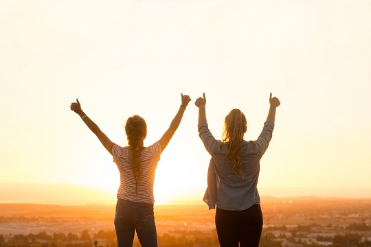 Two young women giving a thumb’s up to the sky