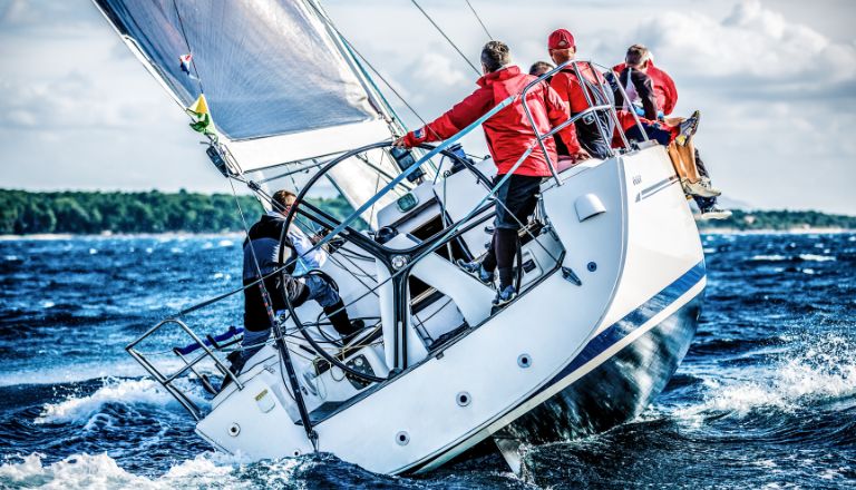Male sailboat crew dressed in red navigate choppy seas.