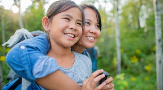 A mother hugging her daughter in a forest setting.