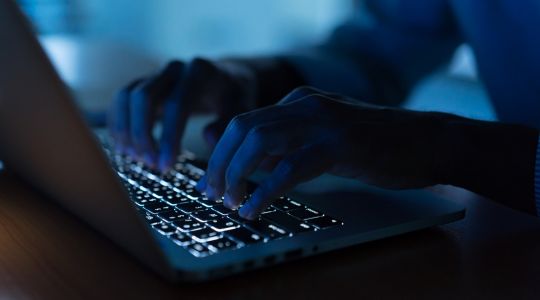 Les mains d'un homme tapant sur un clavier dans une pièce faiblement éclairée.