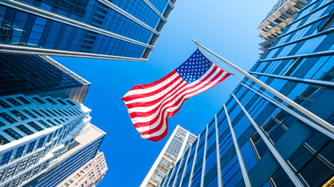 Drapeau américain agitant dans le vent avec l'architecture contemporaine en verre du quartier financier de New York en arrière-plan.