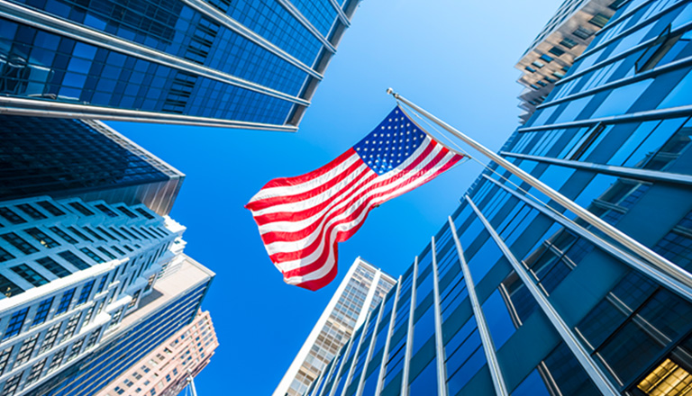 USA flag waving in the wind with contemporary glass buildings in the background.