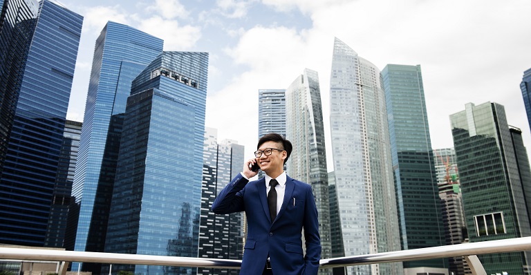 Smiling Asian man stands in front of Bangkok skyscrapers