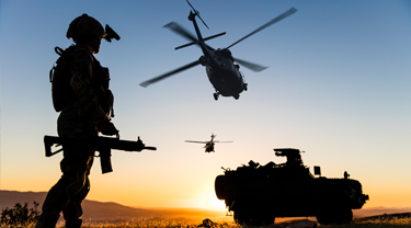 a military man stands at sunset with a helicopter flying overhead