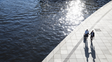 Two business partners walking beside a lake. One man is pulling a suitcase while the other is holding a briefcase.