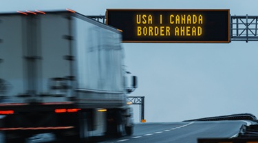 Camion de transport roulant sur l’autoroute et passant sous le panneau annonçant la frontière entre les États-Unis et le Canada.