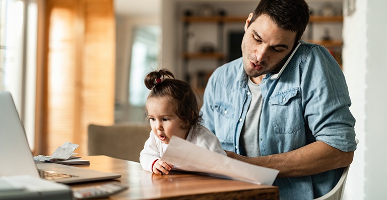 A businessman is working from home while watching his baby girl.